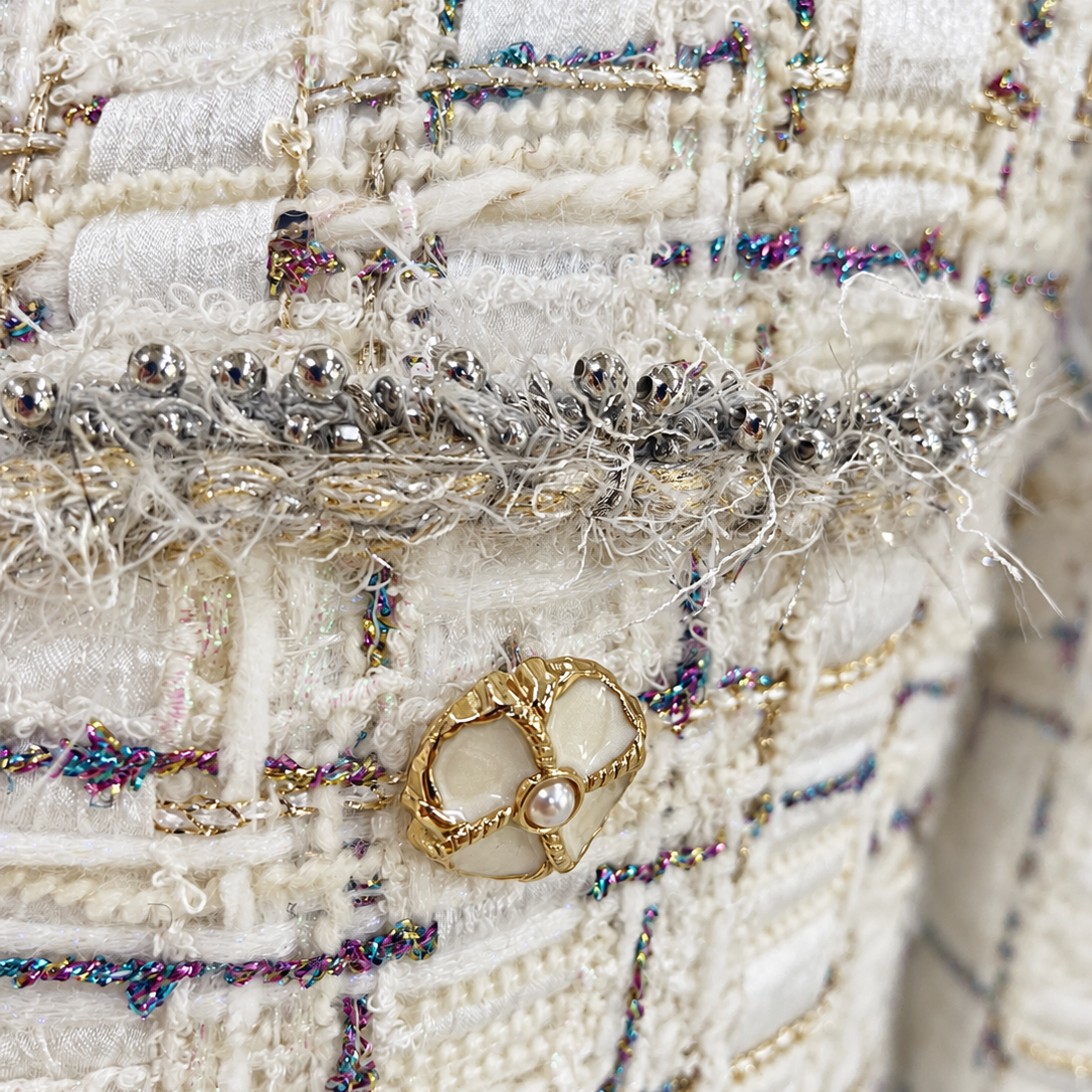 Gold-tone floral button and fringe-trimmed patch pocket on ivory tweed jacket
