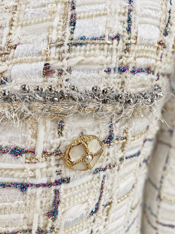 Gold-tone floral button and fringe-trimmed patch pocket on ivory tweed jacket